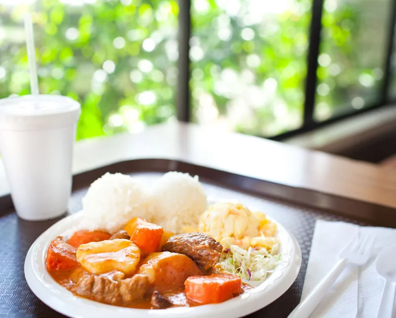 A Cafe 100 beef stew plate with potato and carrot, two scoops of rice, macaroni salad and cabbage.
